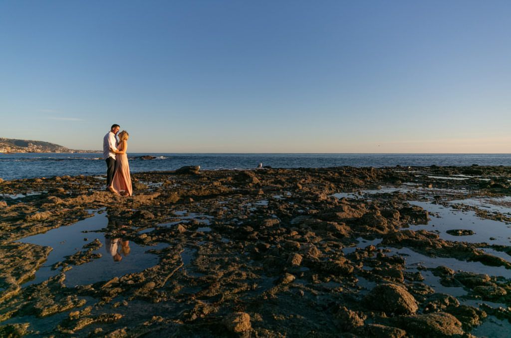 A man and a woman are standing on a rocky beach in Laguna Beach