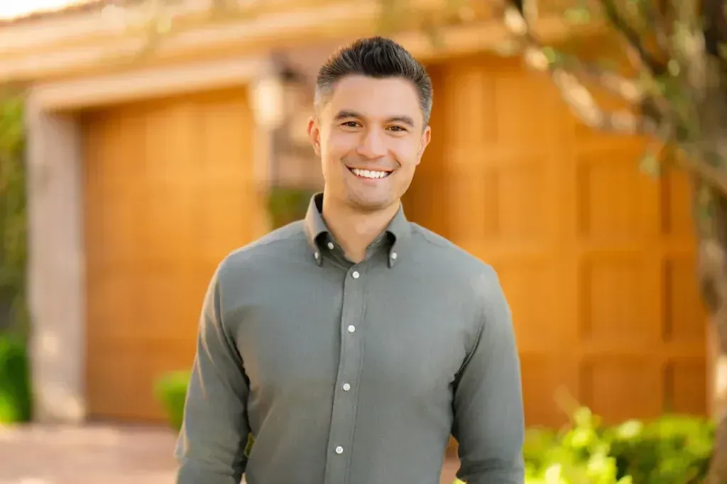 A man in a green shirt is standing in front of a house.