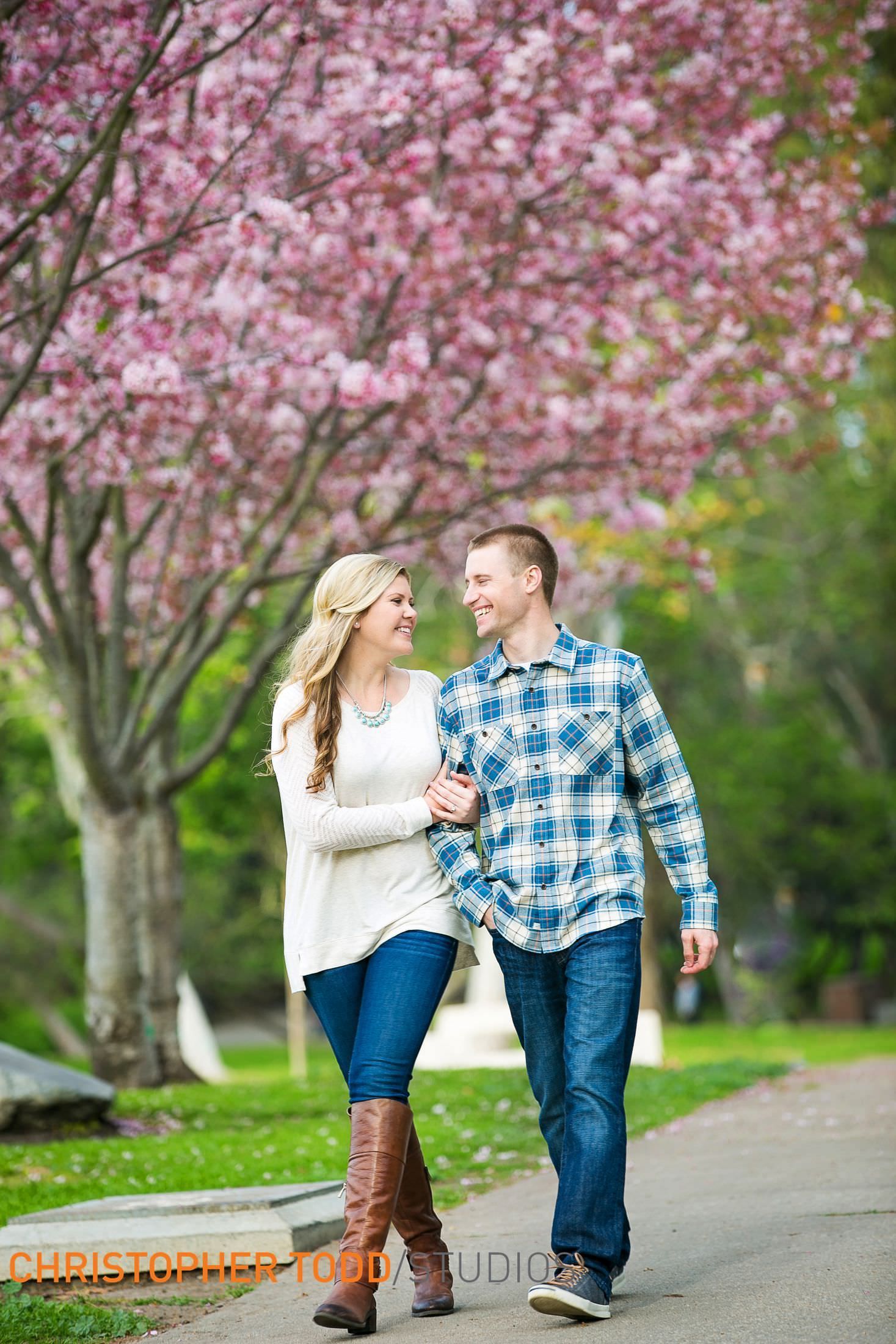 A man and a woman are walking down a path in front of cherry blossom trees in Central Park in Huntington Beach.