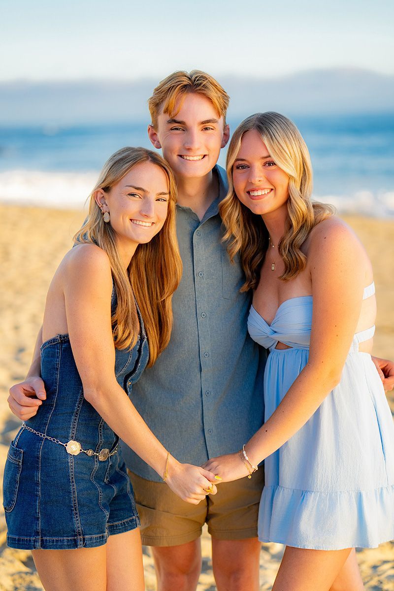 A boy and two girls are posing for a picture on the beach.