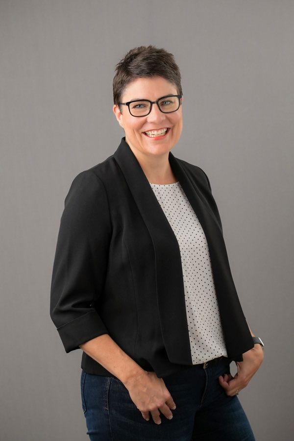 A woman wearing glasses and a black jacket is smiling for the camera.