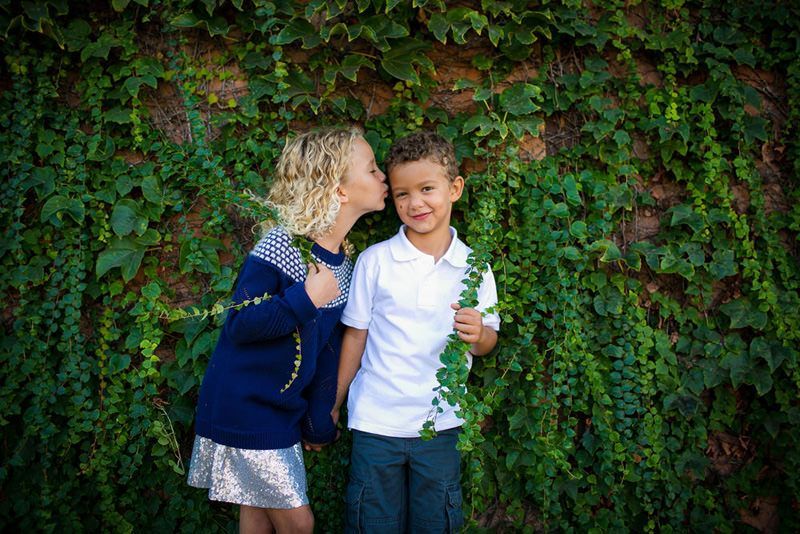 A boy and a girl are standing next to each other in front of a ivy covered wall.