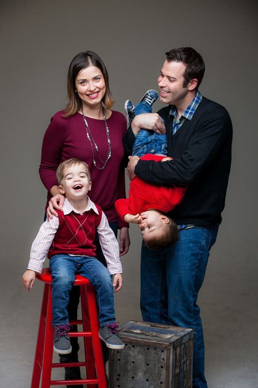 A family is posing for a picture with two children sitting on red stools.