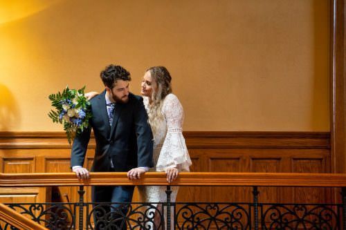 A bride and groom are standing on a balcony looking at each other.