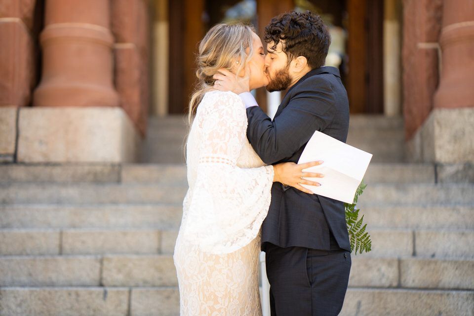 A bride and groom are kissing on the steps of the old courthouse in Orange County, CA