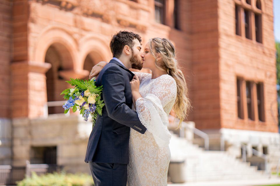 A bride and groom are kissing in front of the Old Courthouse in Orange County