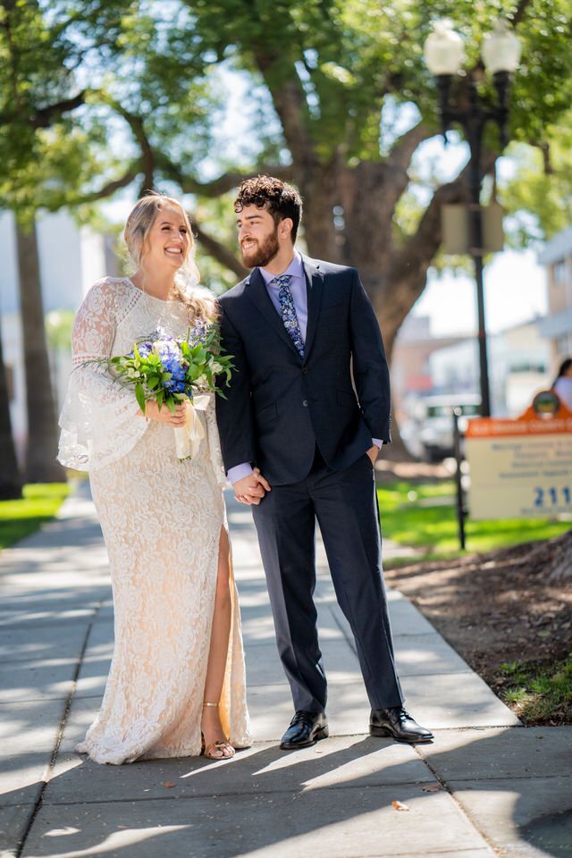 A bride and groom are walking down a sidewalk holding hands at the Old Courthouse in Orange County.
