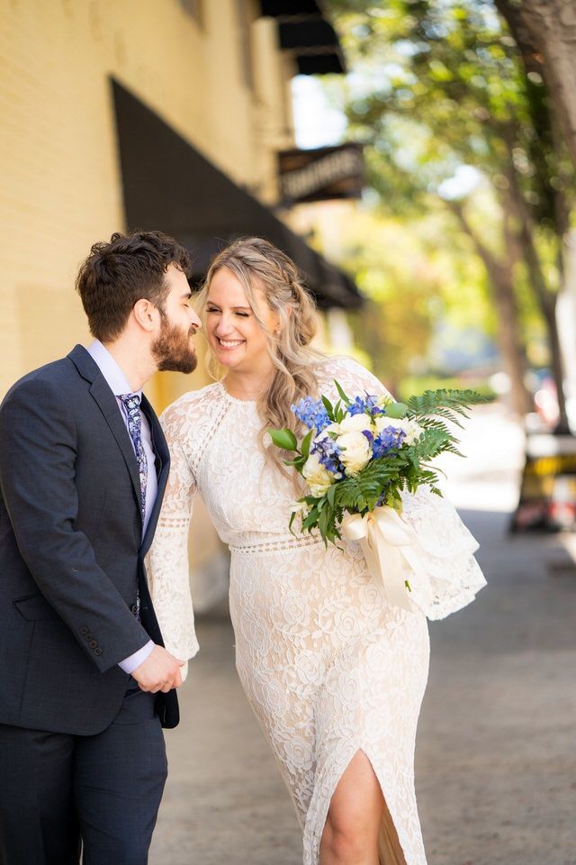 A bride and groom are holding hands and smiling while walking down the street.
