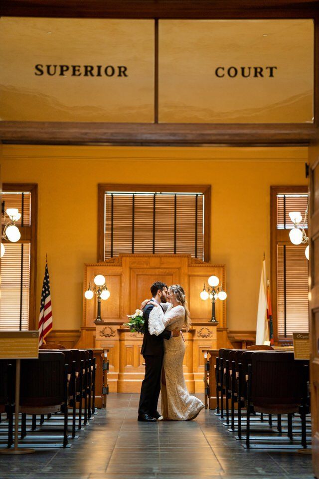 A bride and groom are kissing in front of a superior court at the Old Courthouse in Orange County