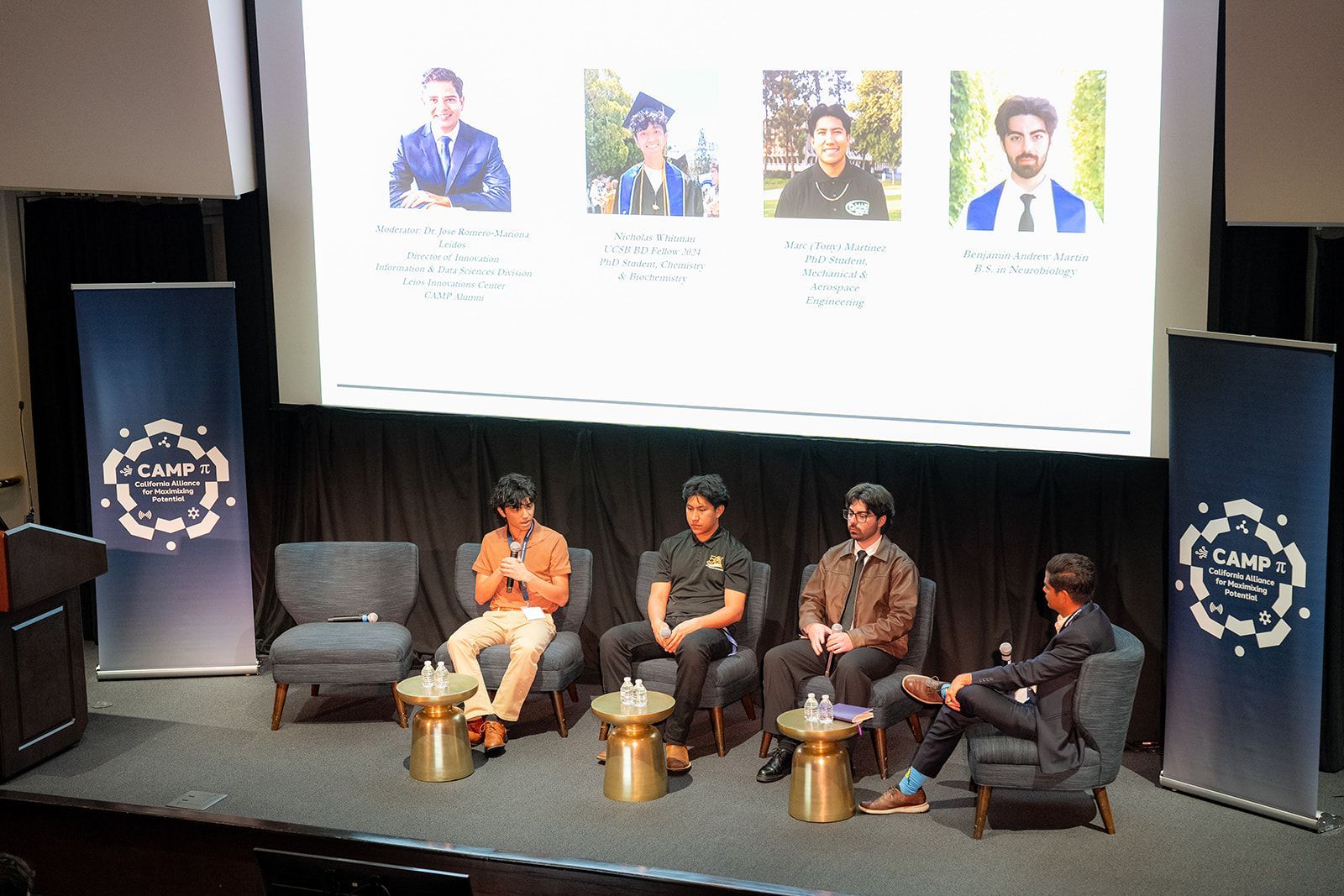 Panel discussion on stage with four seated speakers beneath a projected presentation screen at UCI symposium