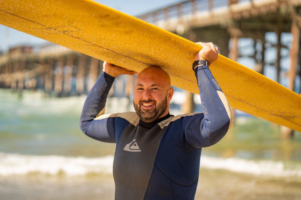 A man in a wetsuit is carrying a surfboard over his head in Newport Beach.