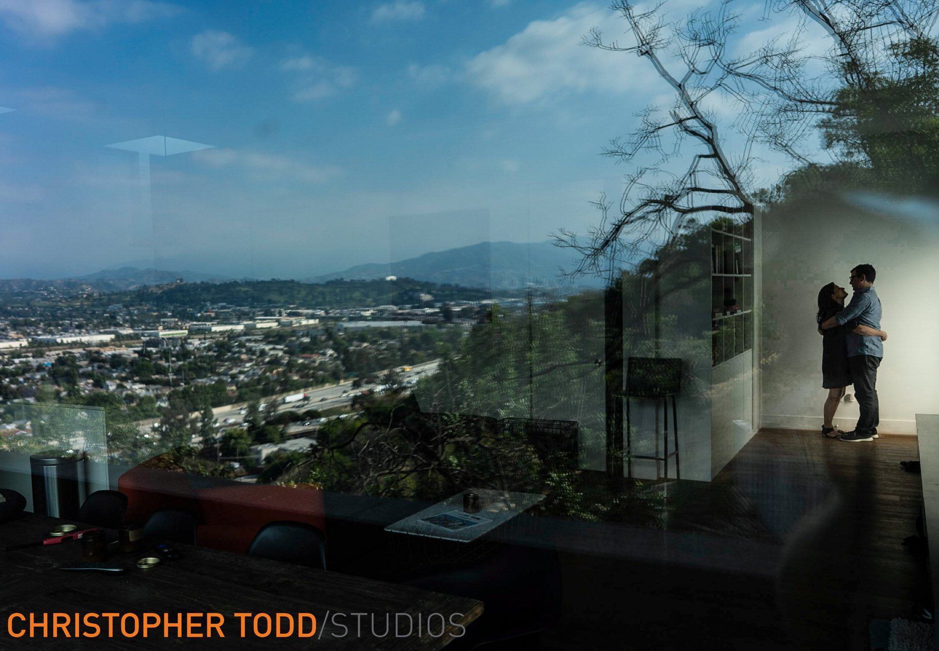 A man and woman are hugging in a room with a view of a city.