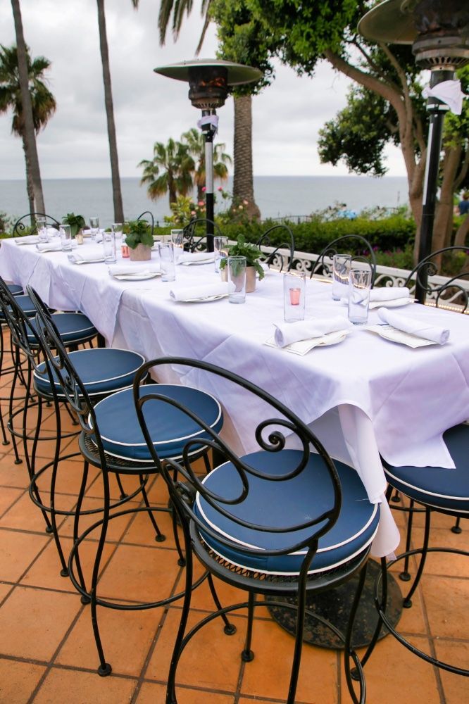 A outdoor patio table with a white table cloth and blue chairs