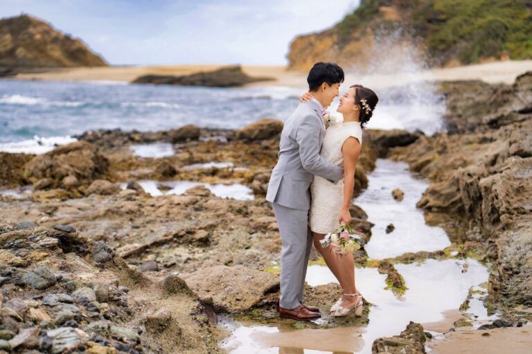 A bride and groom are kissing on a rocky beach under Las Brisas in Laguna
