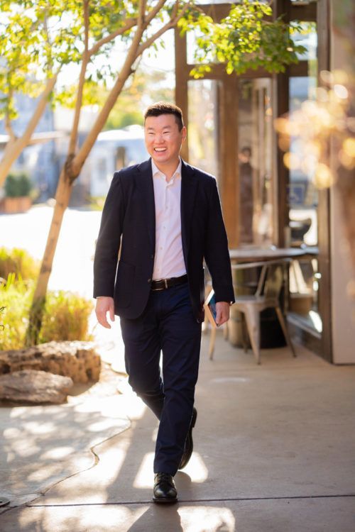 A man in a suit and white shirt is walking down a sidewalk on a dating app photoshoot