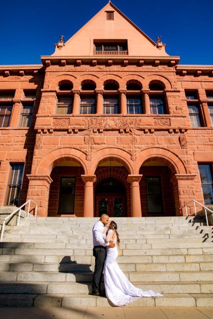 A bride and groom are kissing on the steps of the Old Courthouse