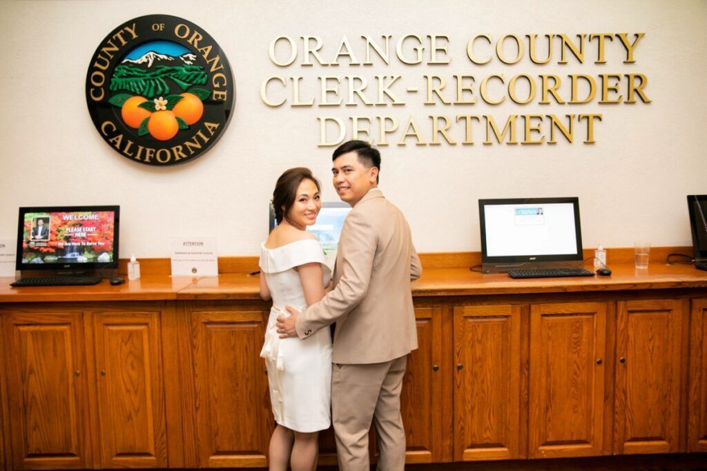 A bride and groom are posing for a picture in front of the orange county clerk recorder at Old Courthouse