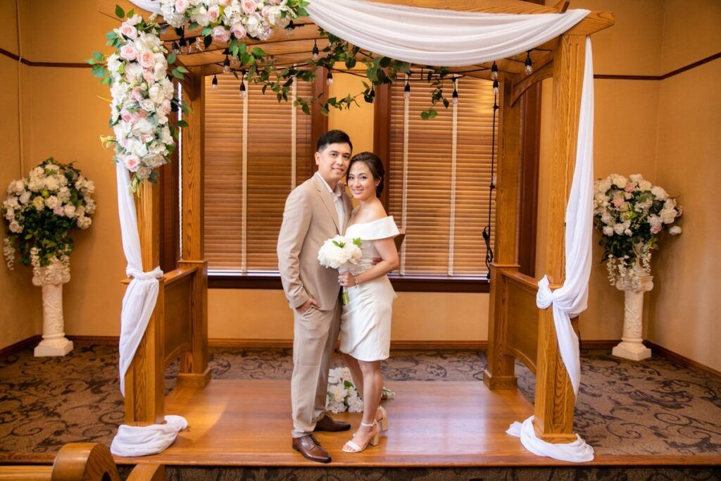 A bride and groom are posing for a picture under a wooden archway at the Old Courthouse.