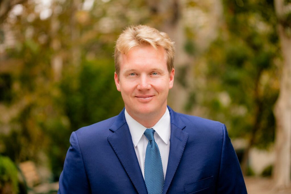 Professional business portrait with A man in a blue suit and tie is smiling for the camera.