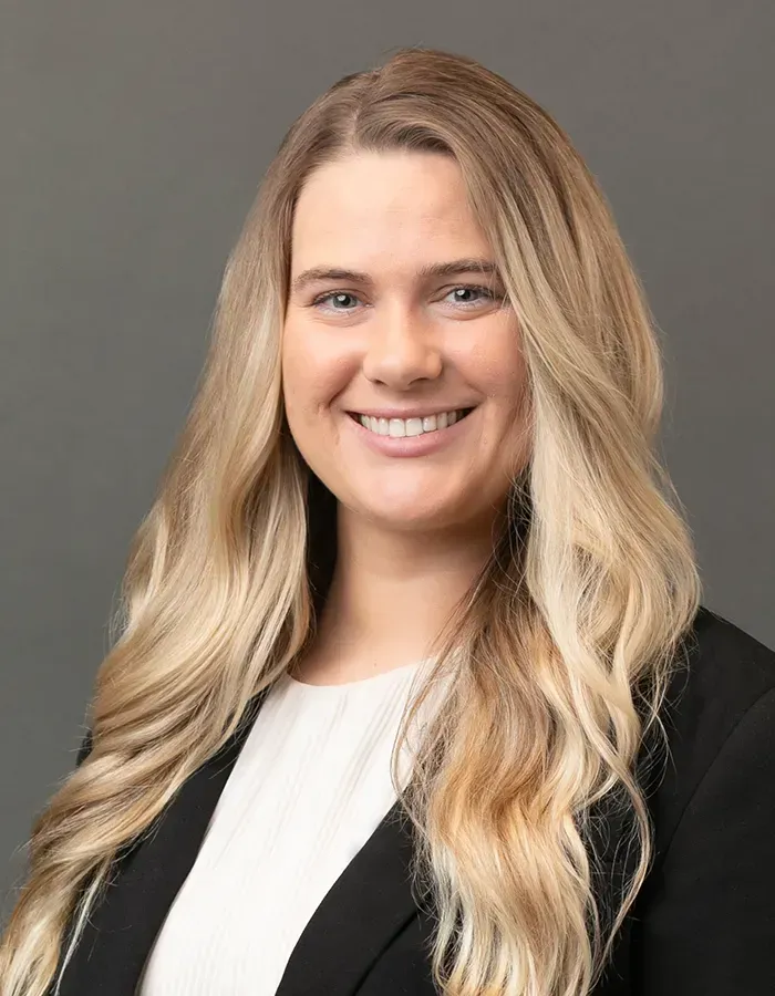 A woman with long blonde hair is wearing a black jacket and smiling for her ERAS photo.