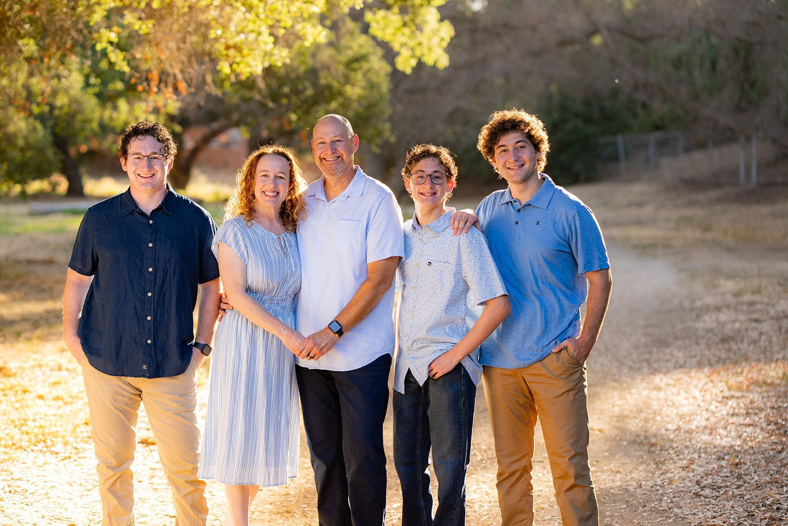 Family of five smiles outdoors, with trees in the background at Hiltshire Trail in Fullerton 