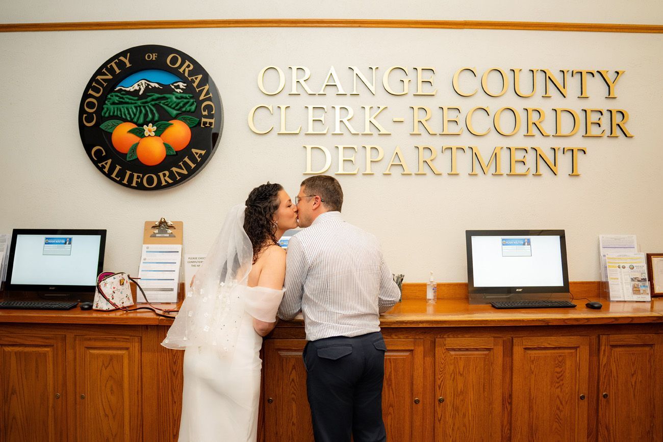 A bride and groom kissing in front of the orange county clerk recorder department as they check in for their civil ceremony