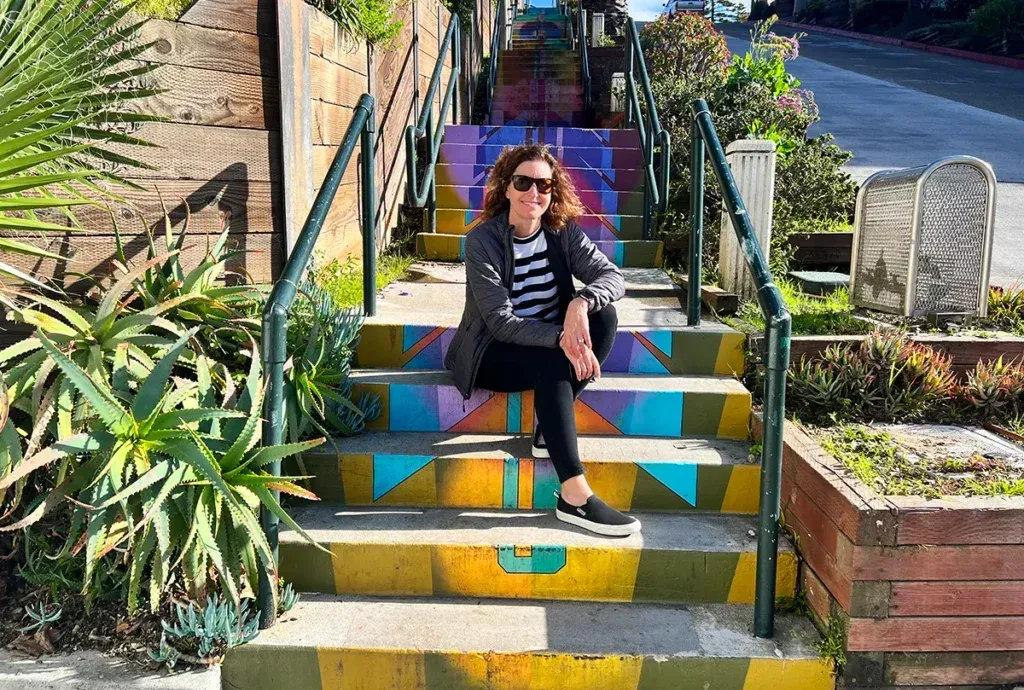 A woman is sitting on a set of colorful stairs in Laguna Beach