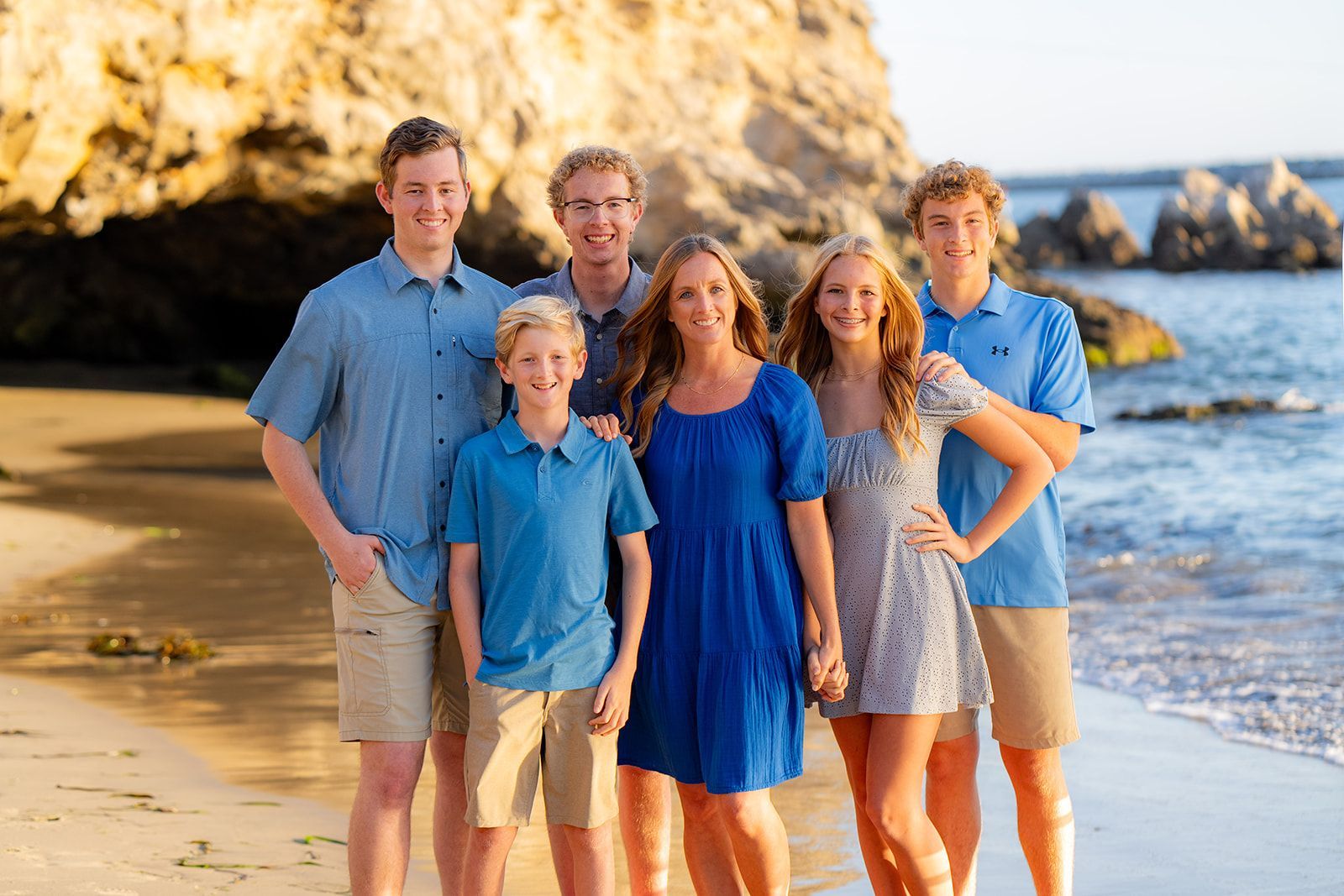 Family of six stands on beach; golden sunlight, blue and white clothing at pirates cove in corona del mar 