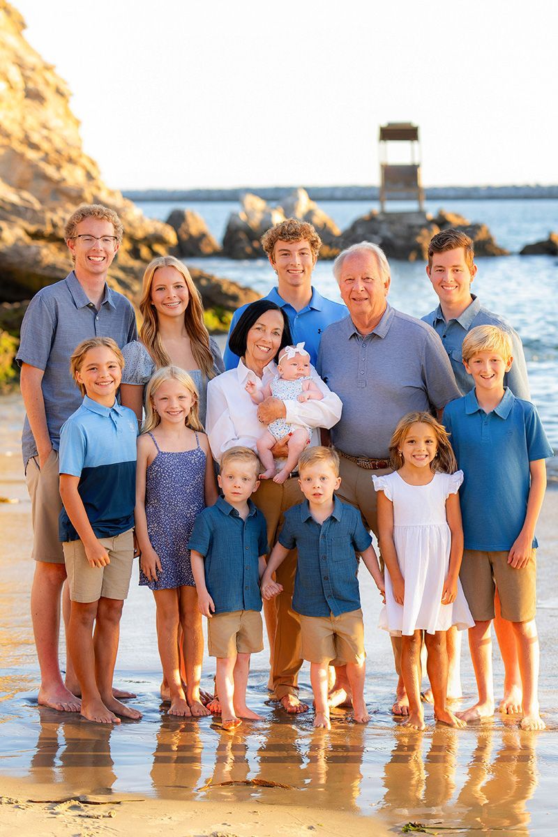 A large family is posing for a picture on the beach.
