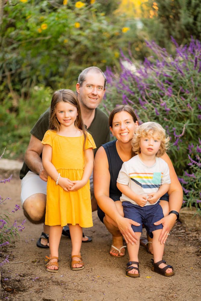 A family is posing for a picture in front of purple flowers.