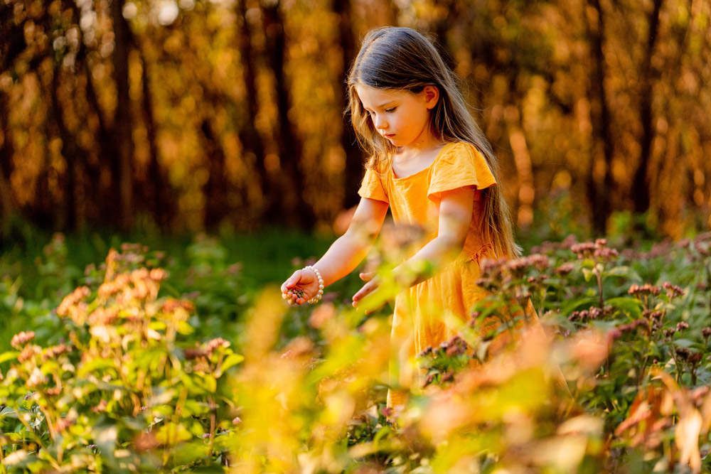 Girl in yellow dress, in a field, touching flowers. Golden sunlight illuminates the scene in Huntington Beach Urban Forest