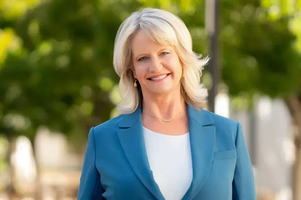 A woman in a blue jacket and white shirt is smiling for the camera.