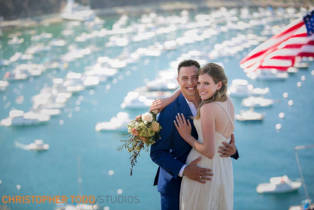 A bride and groom are posing for a picture in front of Avalon Harbor