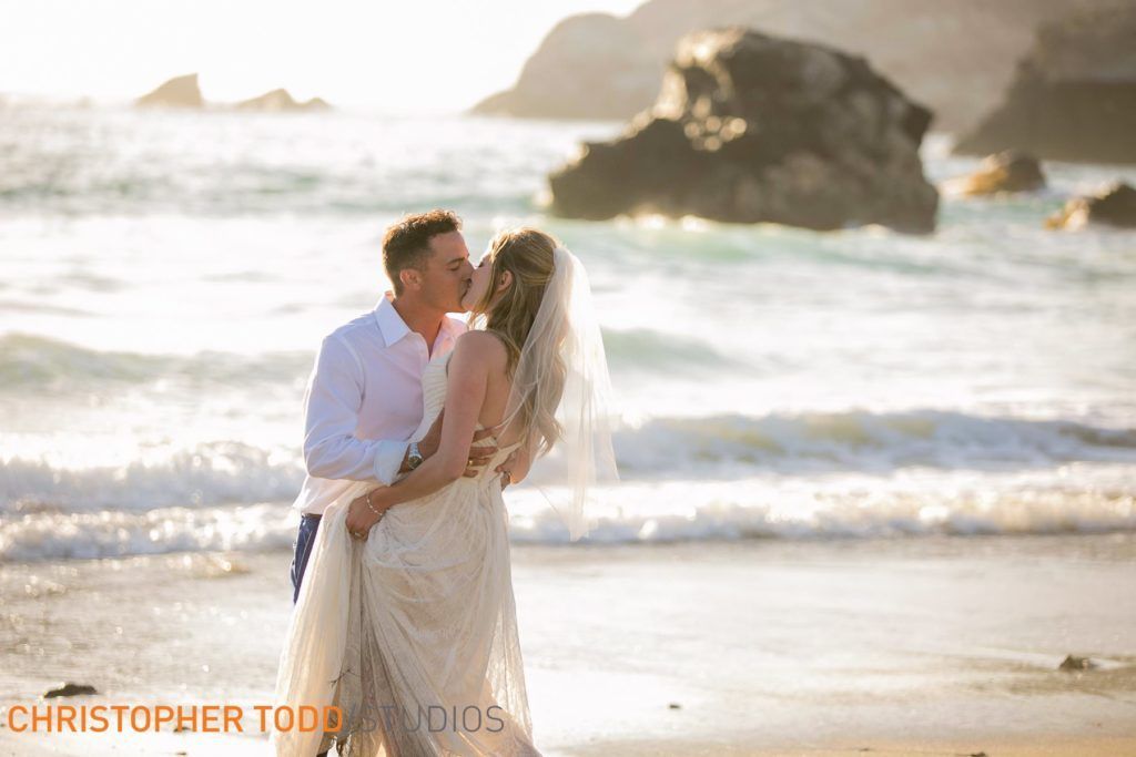 A bride and groom are kissing on the beach in Catalina.