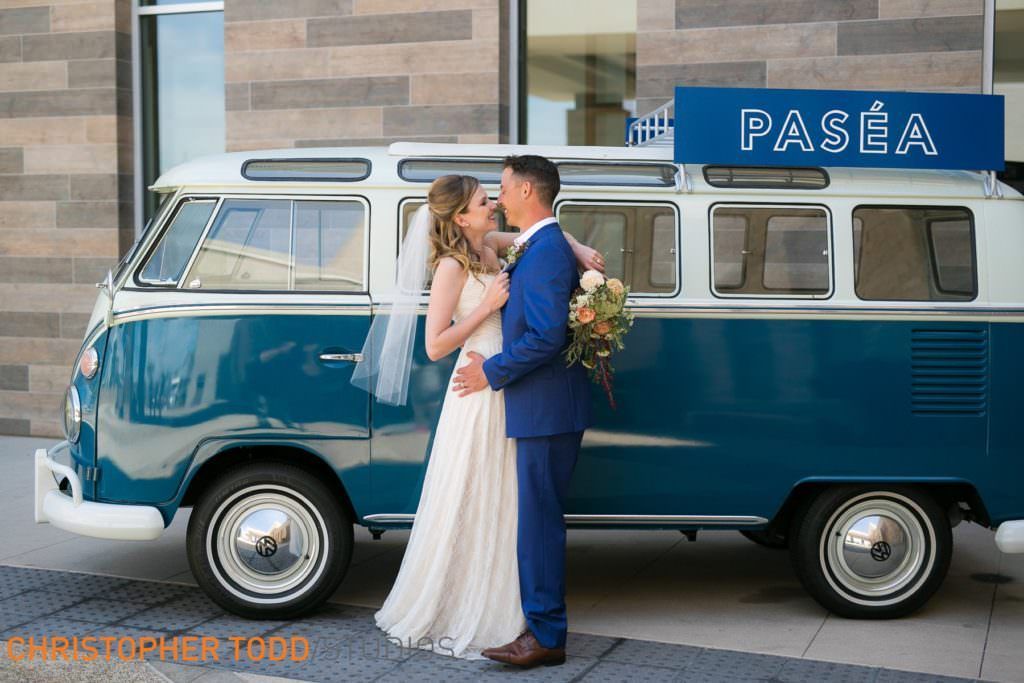 A bride and groom are kissing in front of a blue van in Huntington Beach.