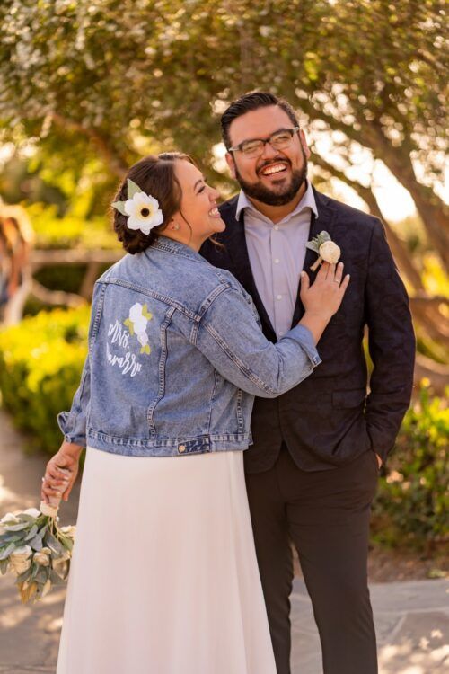 A bride and groom are posing for a picture while the bride is wearing a denim jacket.