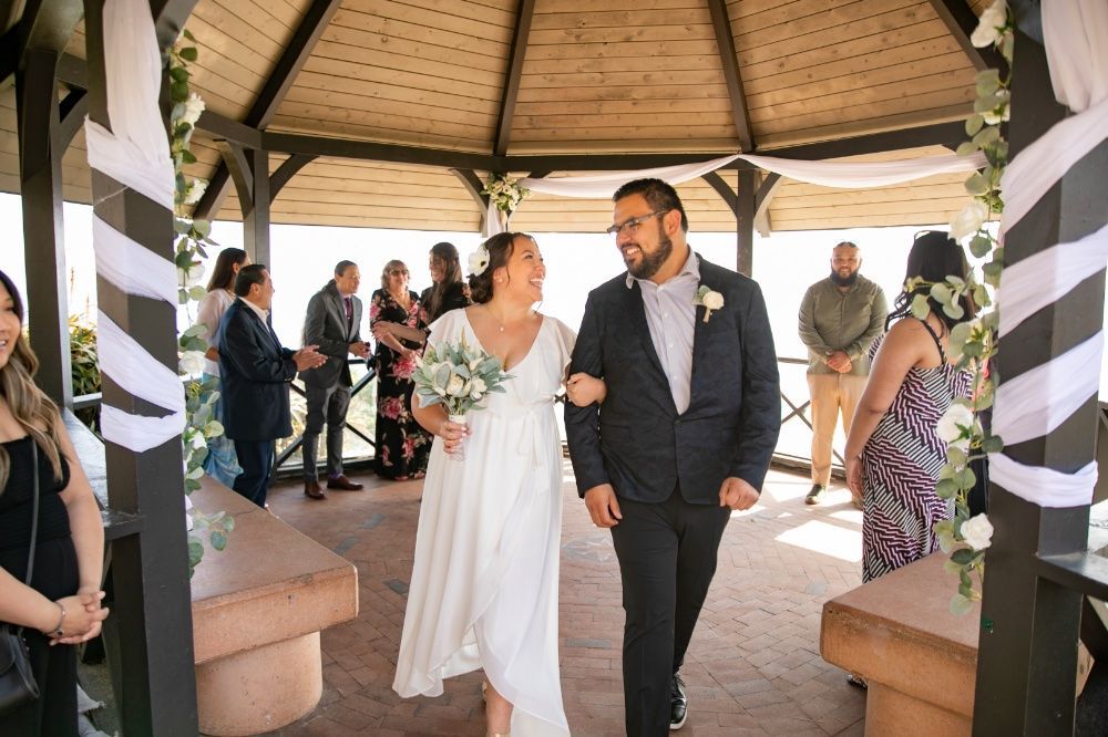 A bride and groom are walking down the aisle at their wedding under a gazebo.