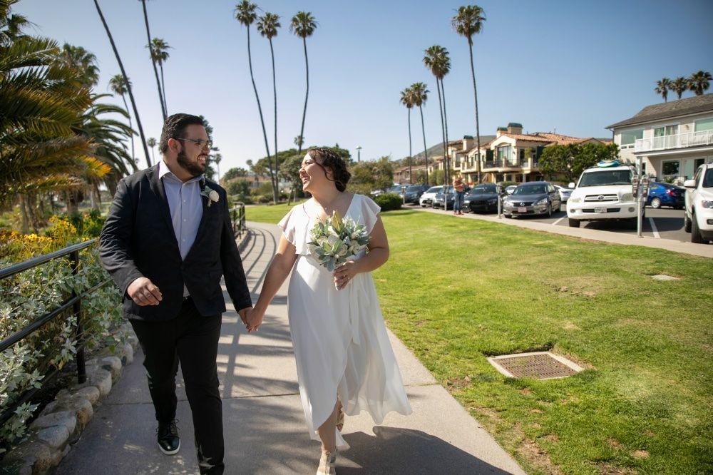 A bride and groom are walking down a sidewalk at Heisler Park in Laguna Beach