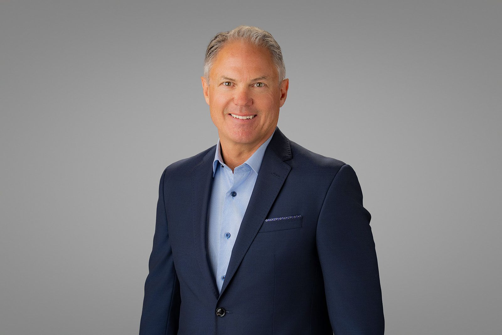 Executive Portraits Photo Day Newport Beach Man in blue shirt and blazer smiling against a gray background in newport beach ca