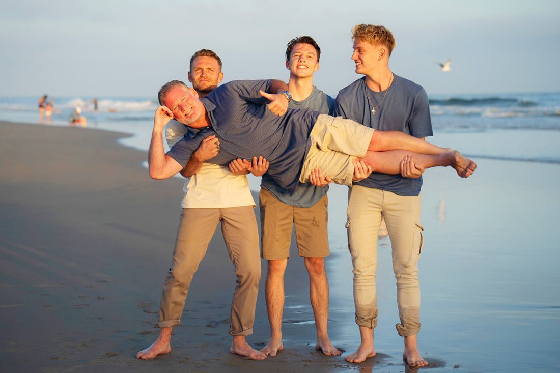 3 sons holding dad in a fun photo at the beach.