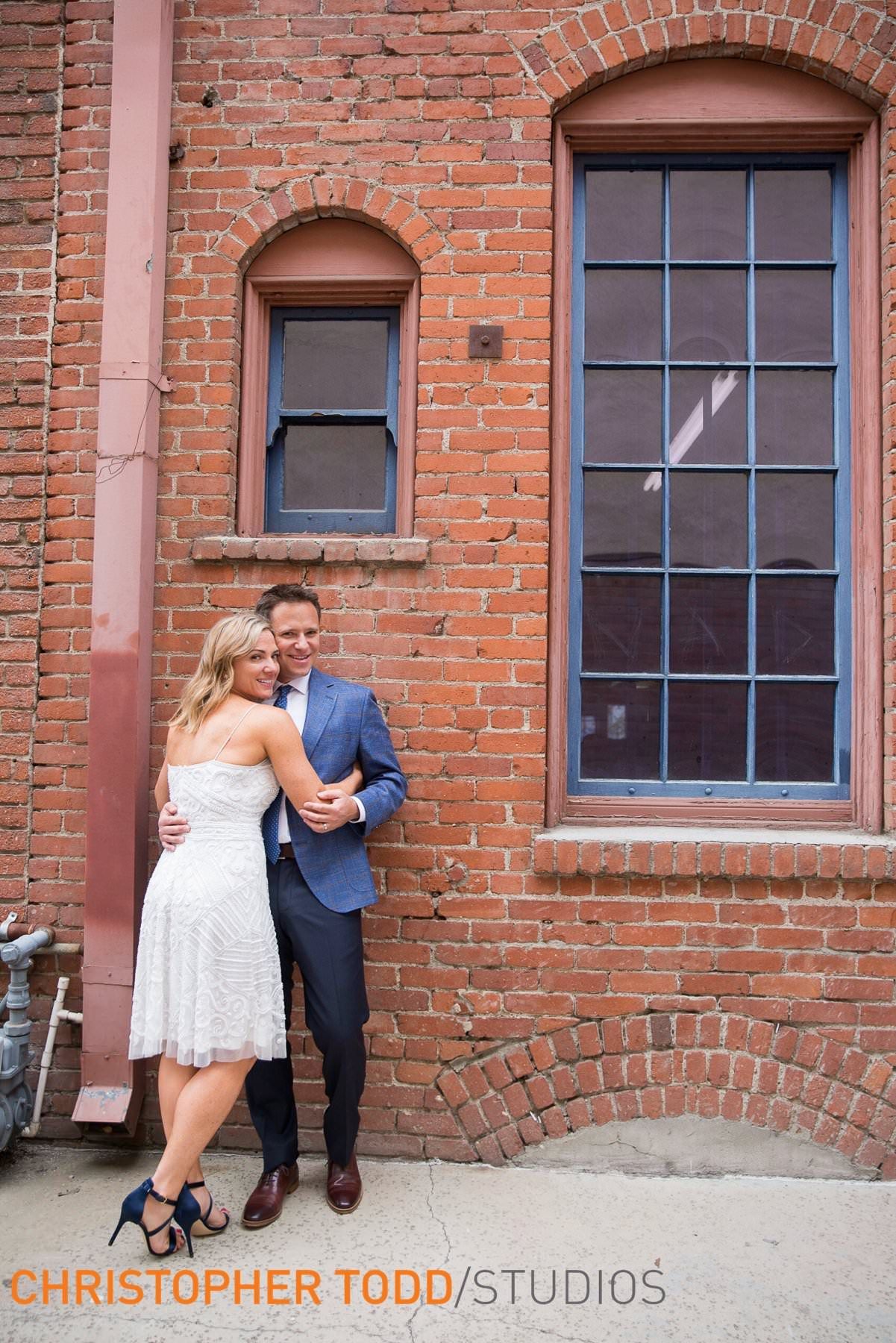 A bride and groom are posing for a picture in front of a brick building.