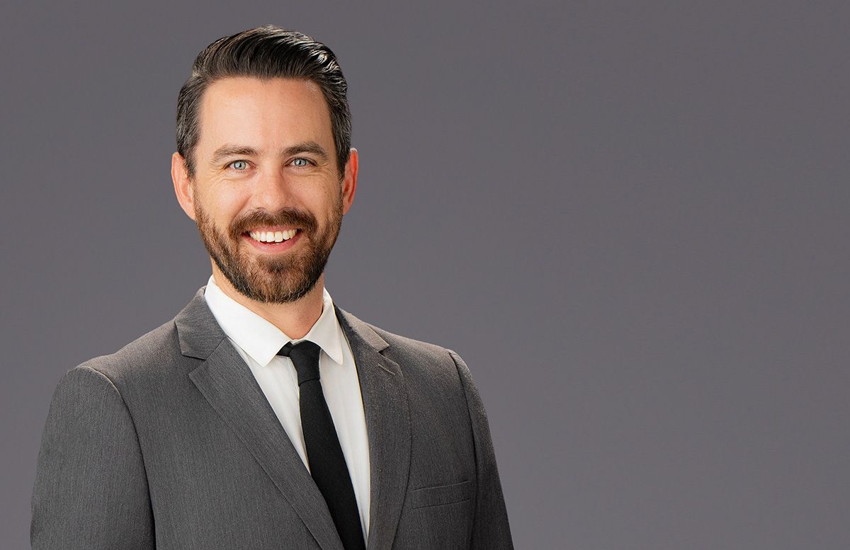 Man in gray suit and tie smiles against a gray background.