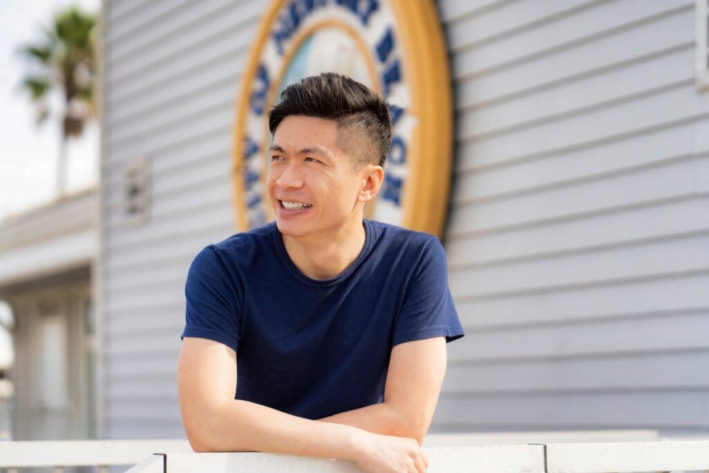 A man in a blue shirt is leaning on a railing in front of a building.