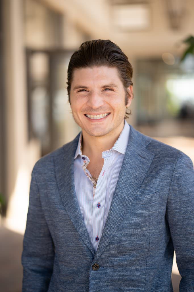 A man in a blue jacket and white shirt is smiling for the camera for a dating app photos.