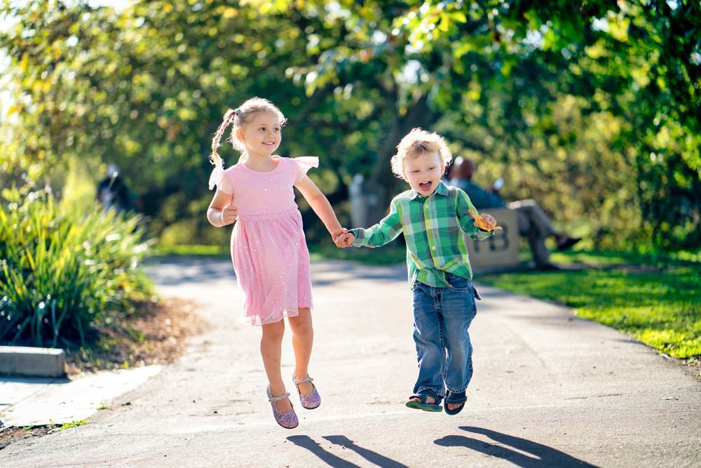 A boy and a girl are jumping in the air while holding hands in Huntington Beach Park.