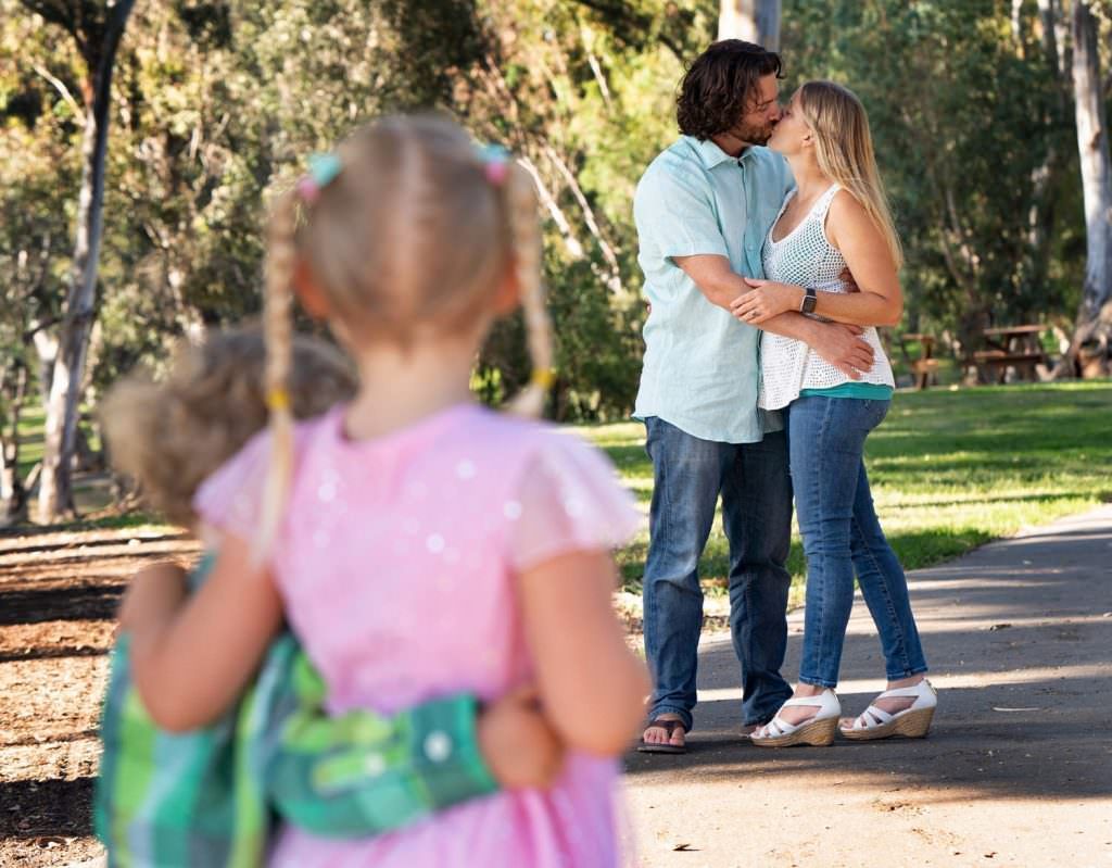 Small children standing in Park Parents in Background kissing
