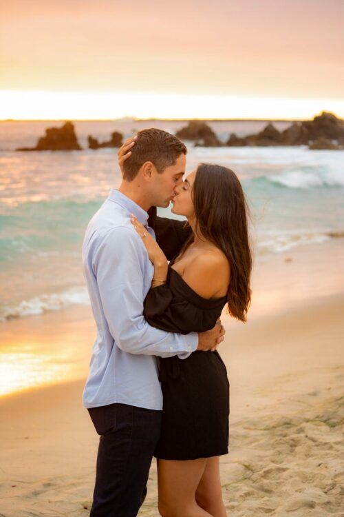 A man and a woman are kissing on the beach at sunset in Orange County.