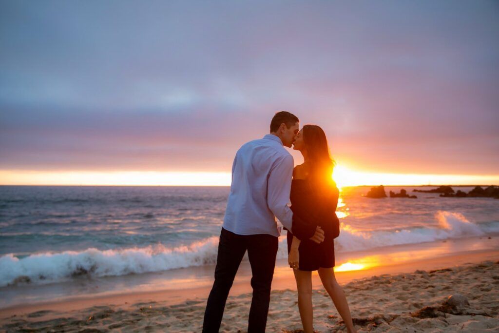 A man and a woman are kissing on the beach at sunset in Orange County.