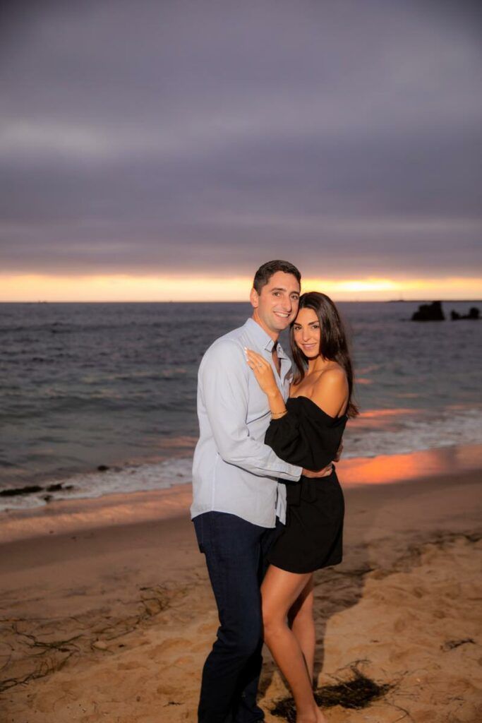 A man and a woman are hugging on the beach at sunset after getting engaged.