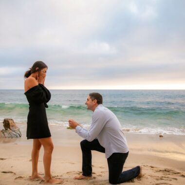 A man is kneeling down to propose to a woman on the beach in Orange County